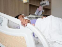 enfoque la mano del paciente en la cama del riel del mango en el hospital con equipo médico foto