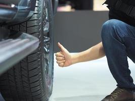 pulgar de la mano del hombre hacia arriba cerca de la rueda grande del coche nuevo foto