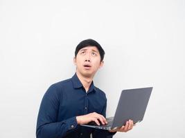 Asian man holding laptop feeling shocked looking up at copy space