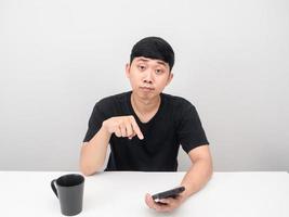 Man point finger at smartphone at the table with coffee cup photo