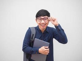hombre asiático con gafas con mochila y sosteniendo una laptop sintiéndose feliz y alegre con un retrato de sonrisa de fondo blanco foto