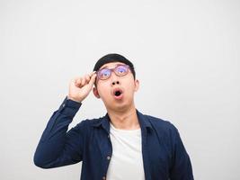 hombre asiático toca sus anteojos sintiéndose asombrado mirando el espacio de copia fondo blanco foto