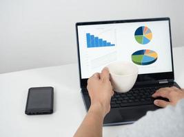 Man hand holding coffee cup and using laptop on the table with mobile phone photo