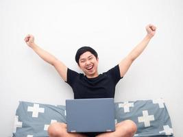 Asian man sitting on the bed with laptop feeling happy and show fist up photo