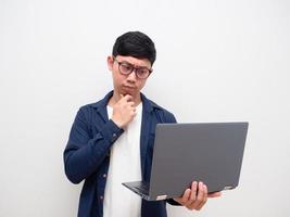 hombre con gafas mirando la computadora portátil en la mano pensando cara seria fondo de pared blanca foto