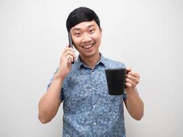 hombre guapo sonriendo sosteniendo una taza de café y hablando con un retrato de teléfono móvil foto