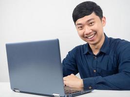 hombre alegre sonriendo sentado con una laptop en el espacio de trabajo de la oficina foto
