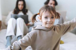 Happy little girl against the background of working parents at laptops at the home photo