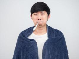 Asian man sick and carry thermometer at mouth cover his body by towel sad face photo