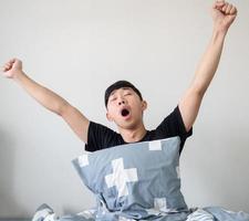 Asian man with pillow wake up at morning and arm up and yawn feel sleepy on white isolated photo