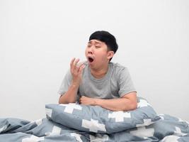 Man sitting on the bed with pillow feel sleepy and yawn photo