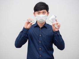 Man wearaing mask show thermometer and infrared thermometer in his hand serious face on white background photo