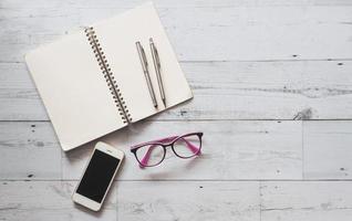 Two silver pen on blank page open notebook with smartphone and glasses on white wood table nature shadow and light top view copy space,Business concept photo