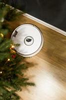 Smart home. Robot vacuum cleaner performs automatic cleaning. Cleans the parquet from Christmas tree needles after the new year. cleans near the Christmas tree after the holidays. photo