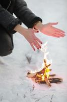 cropped photo of young woman warms her hands over bonfire in winter forest. Close-up