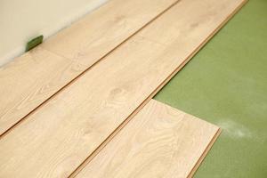 Installing wooden laminate or parquet floor in room over green base. assembling panels quickly and easily - affordable flooring. laying laminate flooring at home photo