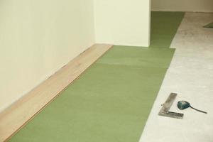 Installing wooden laminate or parquet floor in room over green base. assembling panels quickly and easily - affordable flooring. laying laminate flooring at home photo