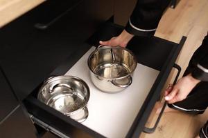 close up of female hand pulls a new stainless steel saucepan out of the kitchen table photo