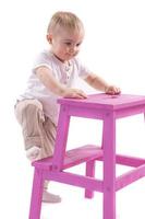 Little boy climbs onto a ladder chair. The beginning of a career concept. Funny little boy isolated on white background. photo