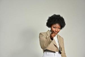 bonita mujer afroamericana con accesorios de moda y peinado afro mirando a la cámara con fondo gris foto