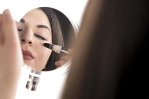 Portrait of a young woman applying liquid make up on her face. Isolated on white background photo