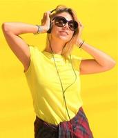 Portrait of happy beautiful blonde girl  hold her wooden longboard skateboard on yellow background wall, look to the camera and smile. Urban scene, city life. Hipster cute lady. photo