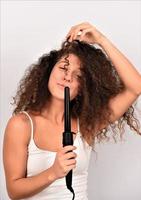 Curly Hair. Beautiful Smiling Woman With Long Wavy Hair Ironing It, Using Curling Iron. Happy Girl With Gorgeous Healthy Smooth Hair Using Curler For Perfect Curls. Hairstyle And Hairdressing photo