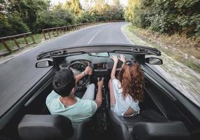 Friends having fun at car trip around the world. Couple in love with arms up on a convertible car. photo