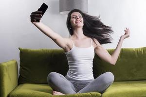 mujer feliz escuchando música desde el teléfono móvil mientras se sienta en la alfombra al lado del sofá en las casas, niña sonriente relajándose con auriculares por la mañana, hora de relajarse. foto