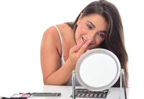 beautiful attractive brunette woman checking her face skin in front of a mirror on white background. photo