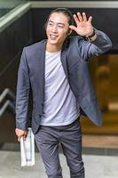 asian male freelancer walking near business center holding phone, smiling reading news, successful businessman photo