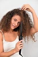 Beautiful Smiling Woman With Long Wavy Hair Ironing It, Using Curling Iron. Happy Girl With Gorgeous Healthy Smooth Hair Using Curler For Perfect Curls. Hairstyle And Hairdressing photo