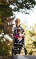 Happy senior lady pushing wheel chair and children. Grandmother and kids enjoying a walk in the park. Child supporting disabled grandparent. Family visit. Generations love and relationship photo