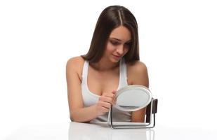 Acne prone skin concept. Young woman looking at mirror at home, checking her face skin photo