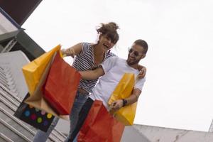 Portrait of cheerful Caucasian young couple man and woman holding many paper bags after shopping while walking and talking on street. Happy family couple with packages outdoor. Buying concept photo