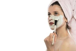 Beautiful woman having clay facial mask apply by beautician. photo