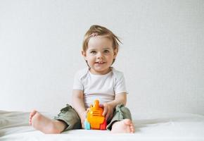 Cute happy funny baby girl in home clothes playing with cat toy on bed at home photo