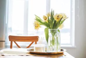 hermoso ramo de tulipanes amarillos en un jarrón en la mesa de la cena en el interior de la cocina blanca en casa foto