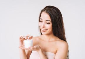 Beauty portrait of happy smiling asian woman with dark long hair put day nourishing moisturizer cream on clean fresh skin face and hands on white background photo