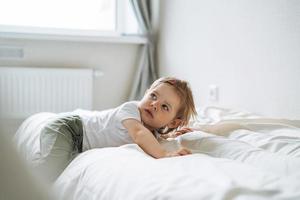 Cute funny baby girl in home clothes lies on bed at home photo