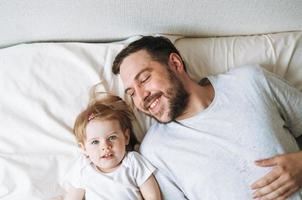 joven familia feliz con padre e hija niña en la cama en un hogar acogedor, vista desde arriba foto