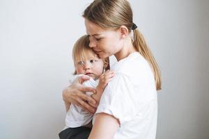 Portrait of young woman mother kissing baby girl daughter on hands at home photo