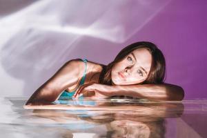 retrato de belleza con agua de una joven modelo de moda con cabello largo oscuro saludable sobre fondo púrpura foto