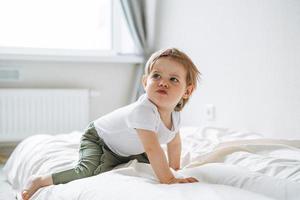 Cute upset baby girl angry child in home clothes sitting on bed at home photo