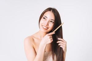 retrato de belleza de mujer asiática sonriente feliz con cabello largo oscuro peinando peine de madera sobre fondo blanco aislado foto