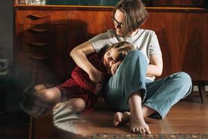 Tween girl and her mother sitting on the floor in living room at home, child looking on reflection photo