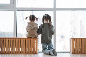 Cute little sisters girls looking in window at home, people from behind photo