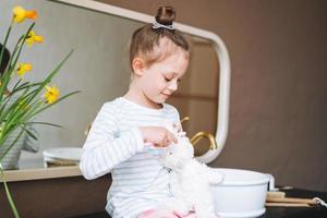 Cute little girl sitting on floor with toy at bright bathroom at home photo