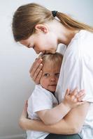 Vertical portrait of young woman mother kissing baby girl daughter on hands at home photo