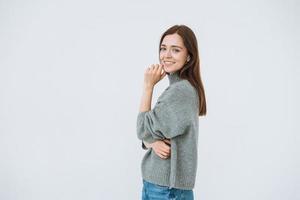 Smiling young woman with dark long hair in grey knitted swaeter on the white background isolated photo